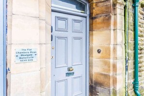 A blue door with a brass knocker, a sign above it, and a stone wall with a green pipe. - Spacious & Characterful 3BED Home in Haltwhistle (Haltwhistle)