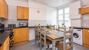 A compact kitchen with wooden cabinets, a built-in oven, a washing machine, and a dining table with chairs. - Sunny, Spacious 3-Bedroom Getaway in Haltwhistle (Haltwhistle)