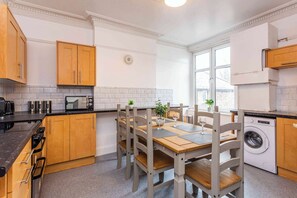 A compact kitchen with wooden cabinets, a built-in oven, a washing machine, and a dining table with chairs.
