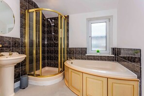 A bathroom with a curved shower enclosure, a freestanding bathtub, a sink, and a window with a view of the outside.