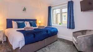 A bedroom with a bed, bedside table, lamp, curtains, and a TV. - Sunny, Spacious 3-Bedroom Getaway in Haltwhistle (Haltwhistle)