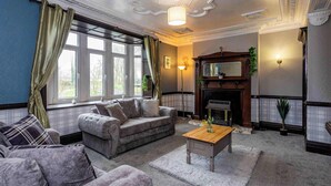 A living room with a fireplace, a sofa, a coffee table, and a window with curtains. - Sunny, Spacious 3-Bedroom Getaway in Haltwhistle (Haltwhistle)