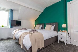 A bedroom with a large bed, a TV, a bedside table with a lamp, and a window with curtains. - Spacious & Characterful 3BED Home in Haltwhistle (Haltwhistle)