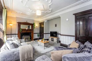 A living room with a fireplace, sofas, a television, and a wooden cabinet. - Spacious & Characterful 3BED Home in Haltwhistle (Haltwhistle)