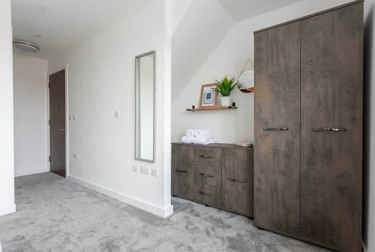 A room with a large wardrobe, a mirror, a shelf with a plant, and a door leading to another room.