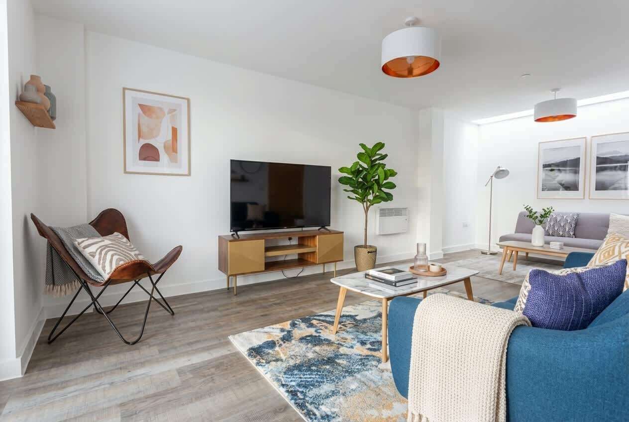 Ett modernt vardagsrum med en platt-TV, en blå soffa, ett soffbord och en mönstrad matta.