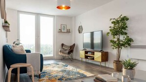 A modern living room with a sofa, a small table, a TV, and a plant. - Modern & Spacious 2BED Apartment by Old Trafford (Manchester)
