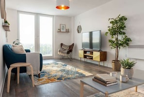 A modern living room with a sofa, a small table, a TV, and a plant. - Modern & Spacious 2BED Apartment by Old Trafford (Manchester)
