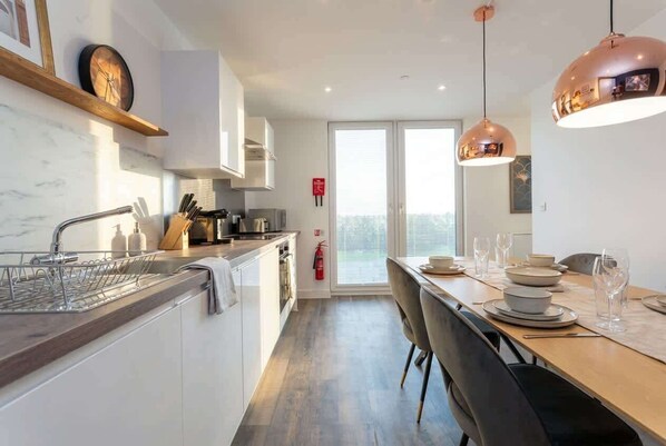 A modern kitchen with a wooden countertop, white cabinets, and a dining area with a table set for two. - Modern & Spacious 2BED Apartment by Old Trafford (Manchester)