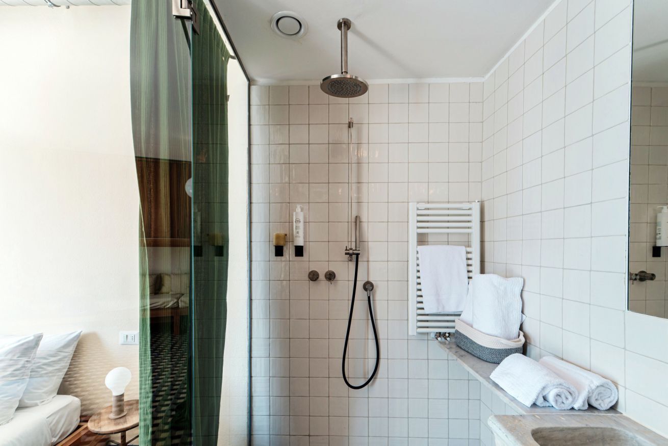 A modern bathroom with a glass shower enclosure, a white tiled wall, a built-in towel rack, and a visible toilet.