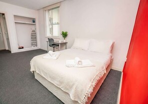 A hotel room with a bed, a desk, a chair, a window, and a plant. - Modern Central Coventry Studio – Gym Access (Coventry)