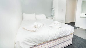 Un letto rifatto con lenzuola bianche, un cuscino a righe e un comodino con una lampada.