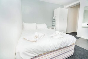 A neatly made bed with white linens, a striped pillowcase, and a small bedside table with a lamp. - Bright & Cosy Studio in Central Coventry (Coventry)