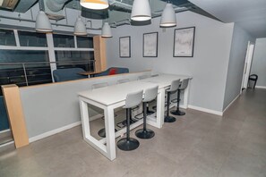 A modern kitchen with white countertops, bar stools, pendant lighting, and framed artwork on the walls. - Bright & Cosy Studio in Central Coventry (Coventry)