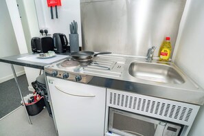 A compact kitchenette with a stove, sink, and a small refrigerator. - Bright & Cosy Studio in Central Coventry (Coventry)