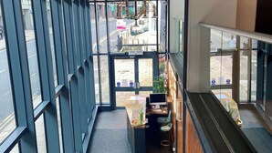 Een modern interieur met een trap, een receptiebalie en grote ramen met uitzicht op de straat.