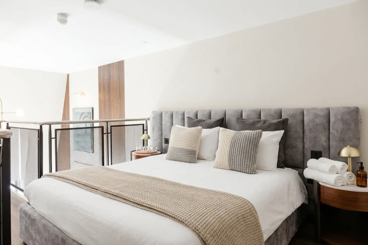A hotel room with a large bed, a bedside table with a lamp, and a view of a balcony.