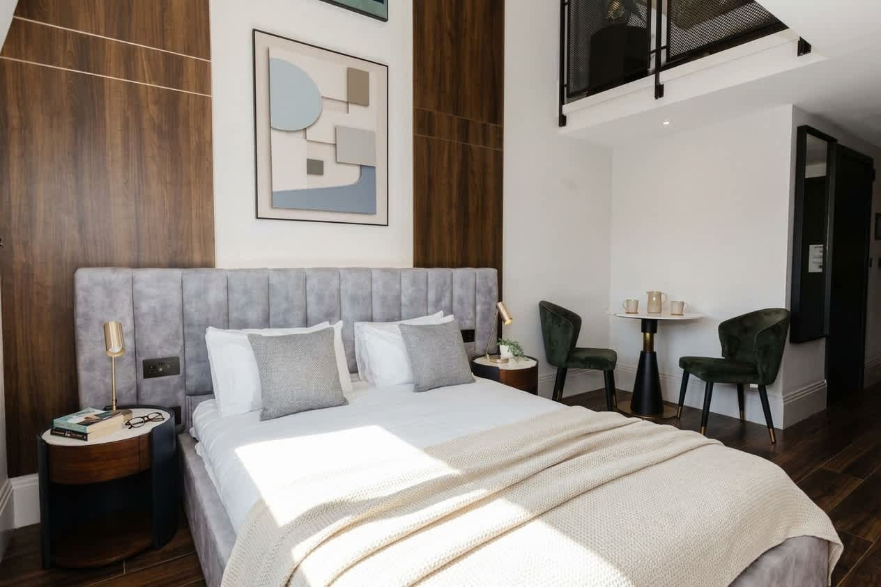 A modern bedroom with a large bed, a side table, a small round table with cups, and a chair.