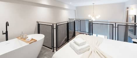 A modern bathroom with a freestanding bathtub, a shower area, and a bed with towels.