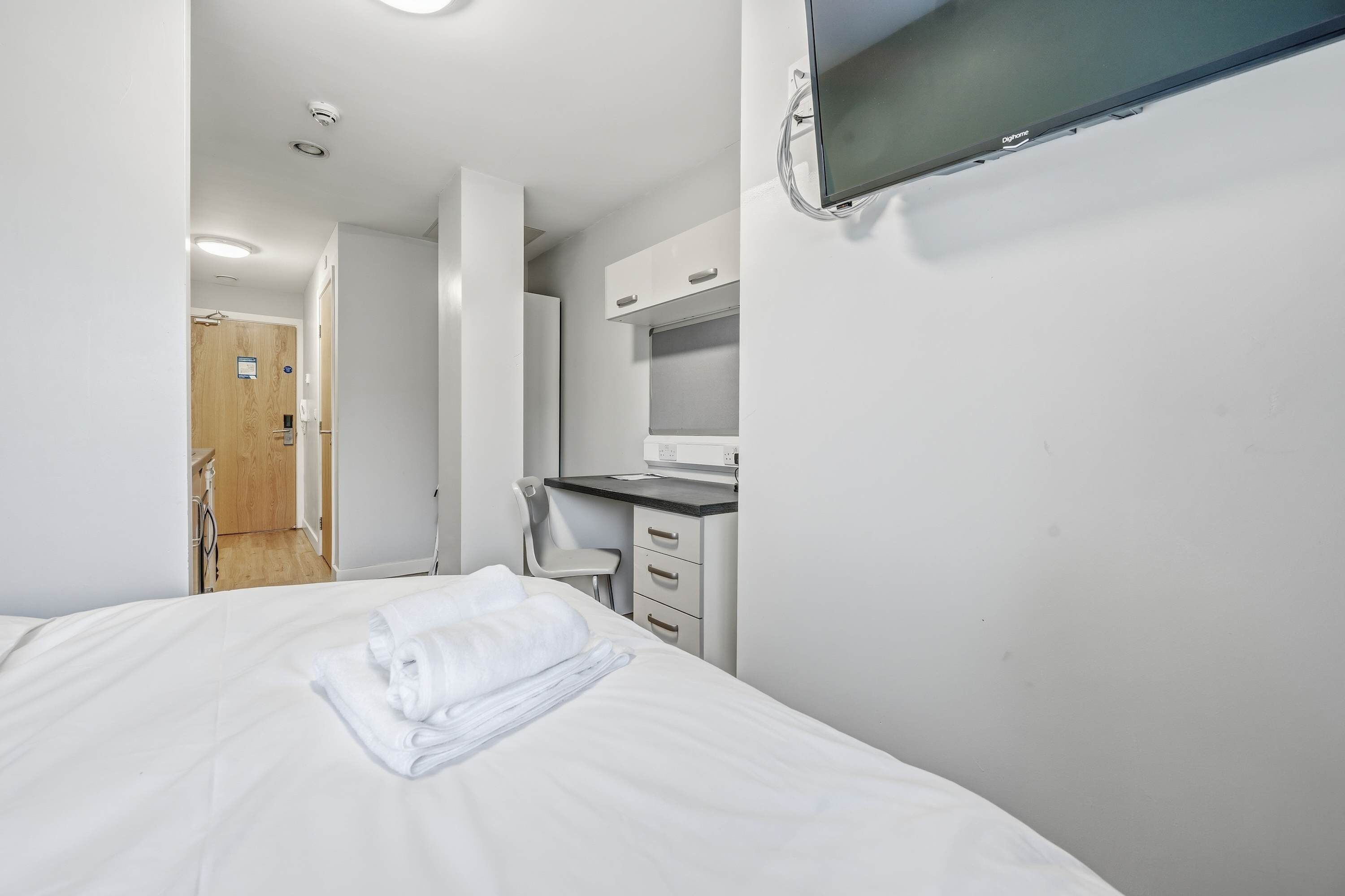 A hotel room with a bed, a desk, a chair, and a television mounted on the wall.
