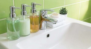 A bathroom sink with three dispensers, a faucet, and a small potted plant. - Cosy Budget Double Studio in Nottingham Centre (Nottingham)