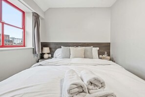 A hotel room with a bed, a nightstand, a lamp, a window with curtains, and a view of buildings outside. - Cosy Budget Double Studio in Nottingham Centre (Nottingham)