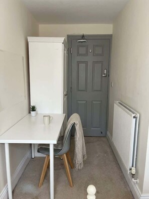 Ein kleiner, schmaler Raum mit einem weißen Tisch, einem grauen Stuhl, einer Heizung und einer grauen Tür.