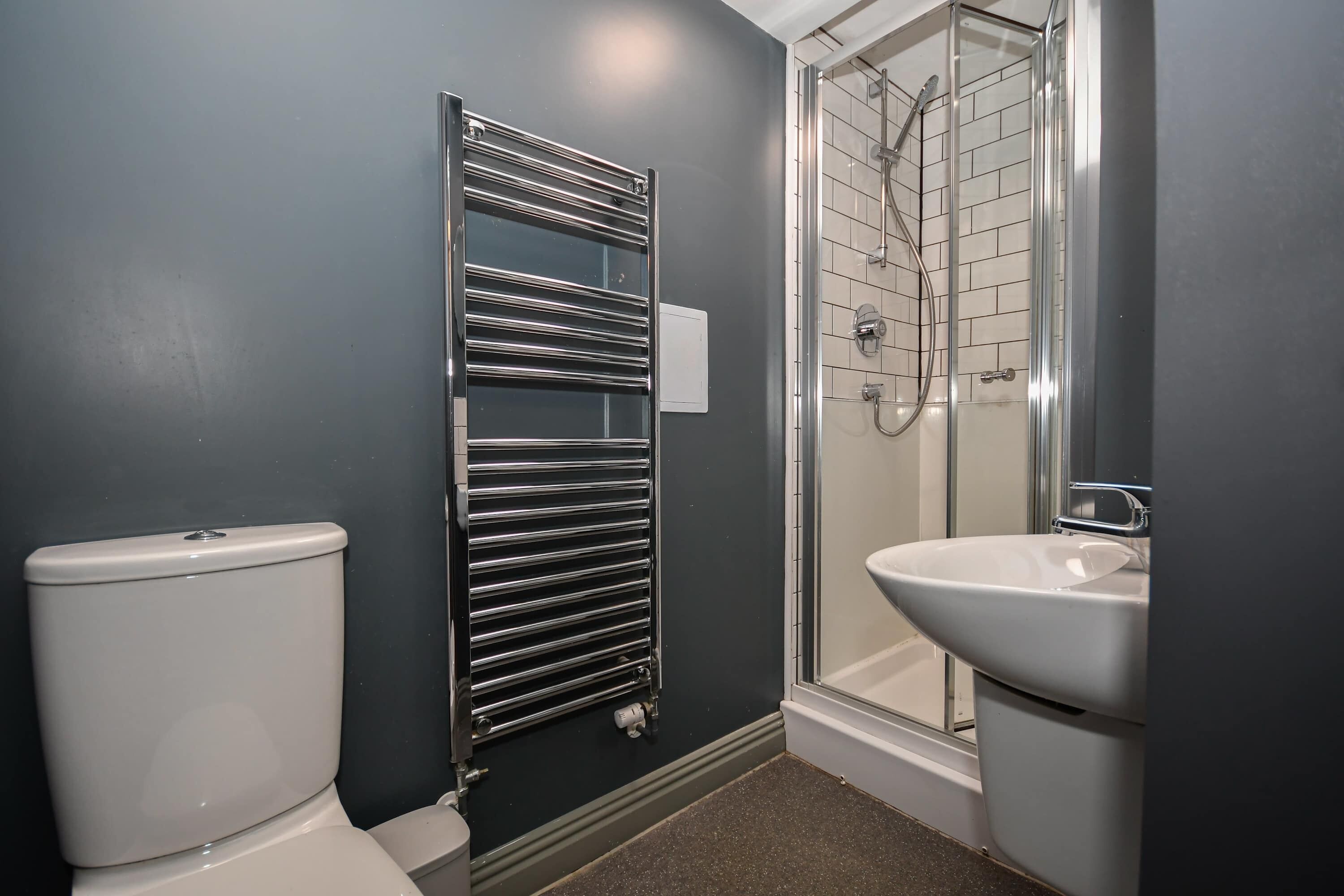 A bathroom with a toilet, a chrome towel rack, a glass shower enclosure, and a sink.