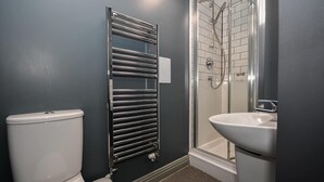 Een badkamer met een toilet, een chromen handdoekrek, een douchecabine met glazen wanden en een wastafel.