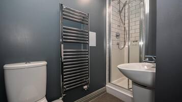 A bathroom with a toilet, a chrome towel rack, a glass shower enclosure, and a sink.