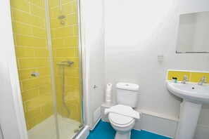 A bathroom with yellow tiles, a white toilet, a shower enclosure, and a sink with a mirror above it. - Convenient Budget Studio in Central Sheffield (Sheffield)