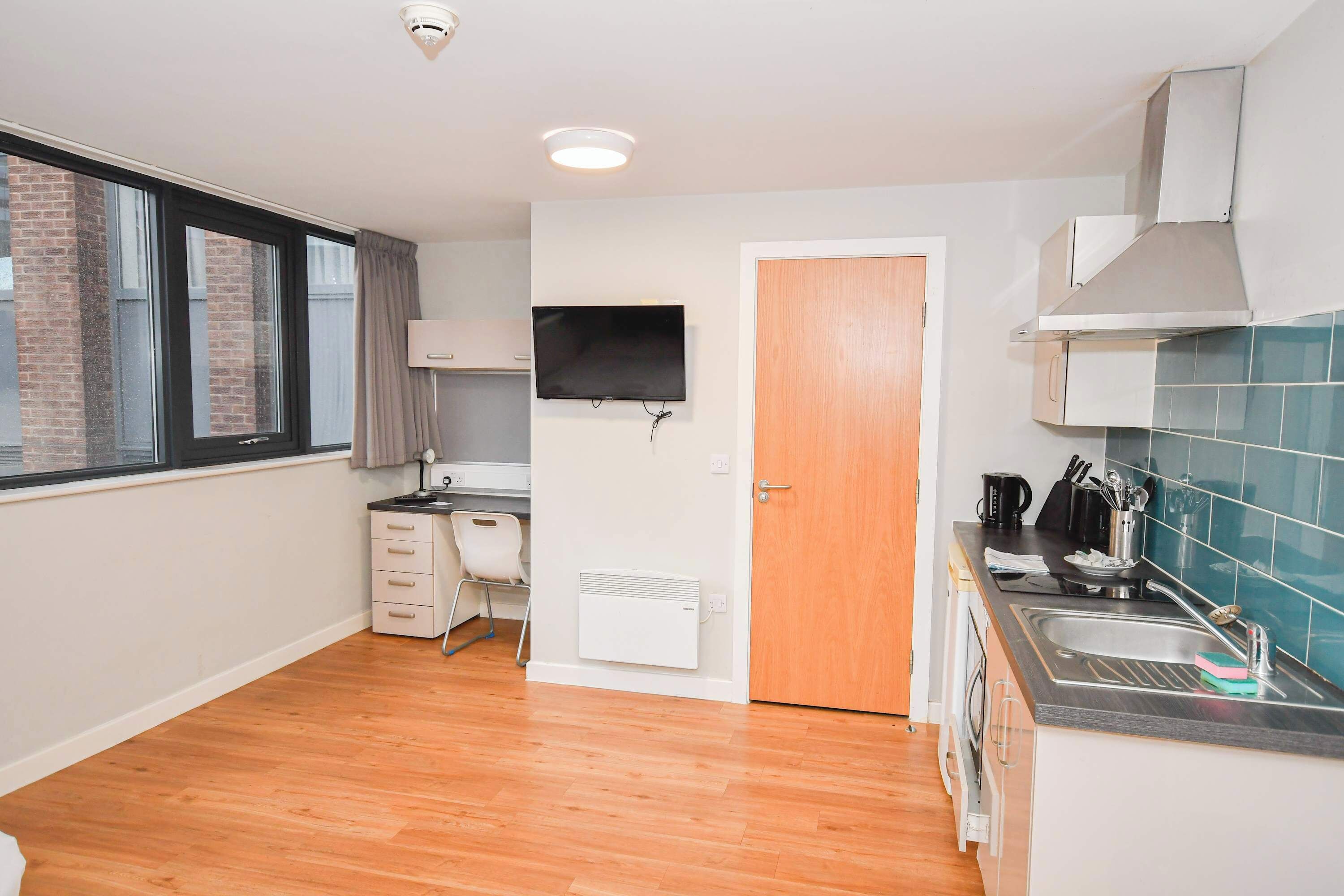 A compact kitchen with a window, a flat-screen TV, a white radiator, and a sink.