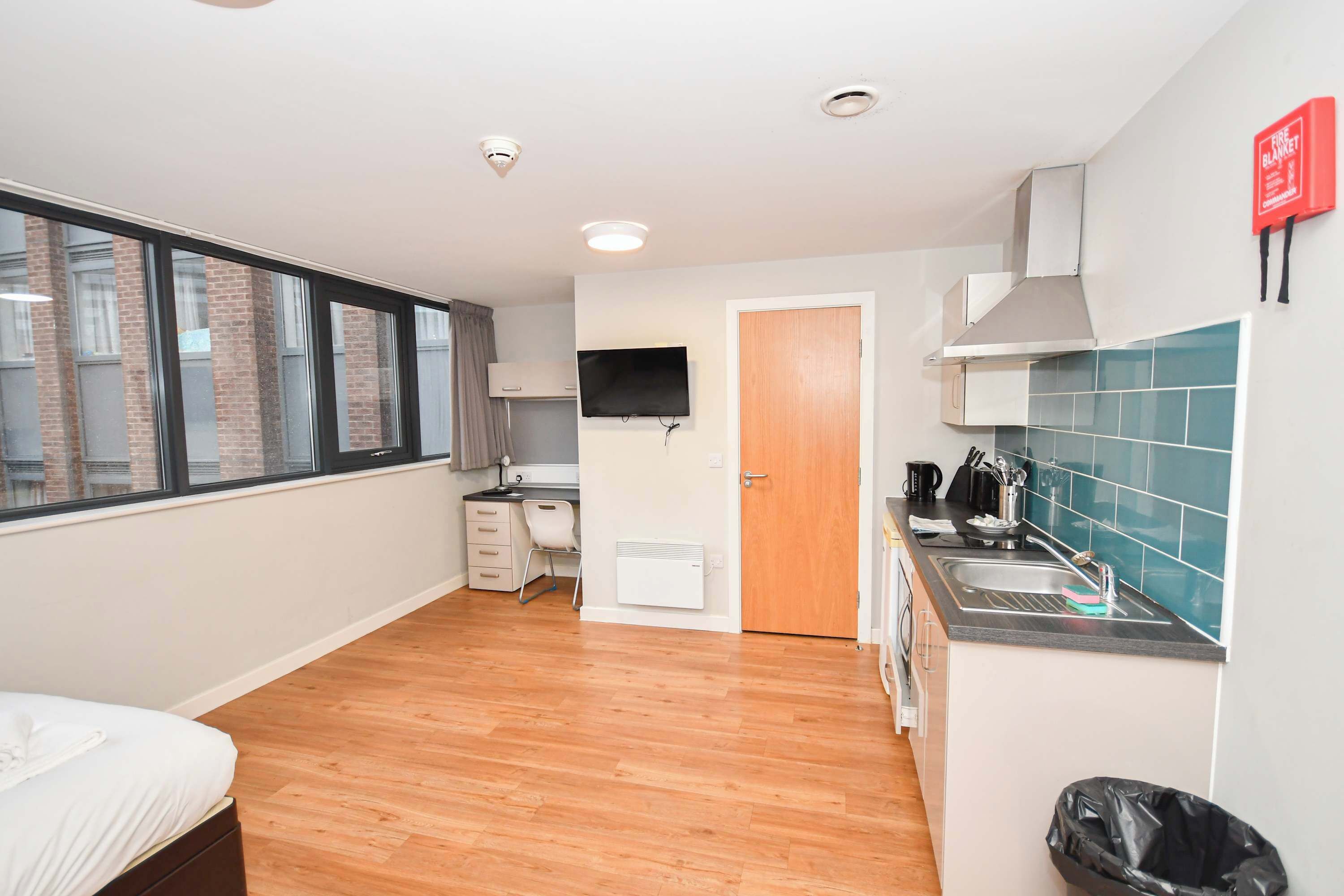 Une chambre d’hôtel compacte comprenant un lit, un bureau, une kitchenette, une télévision et une vue sur la ville.