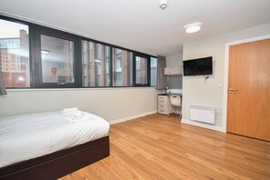 A bedroom with a bed, a desk, a chair, a TV, and a window with a city view. - Convenient Budget Studio in Central Sheffield (Sheffield)