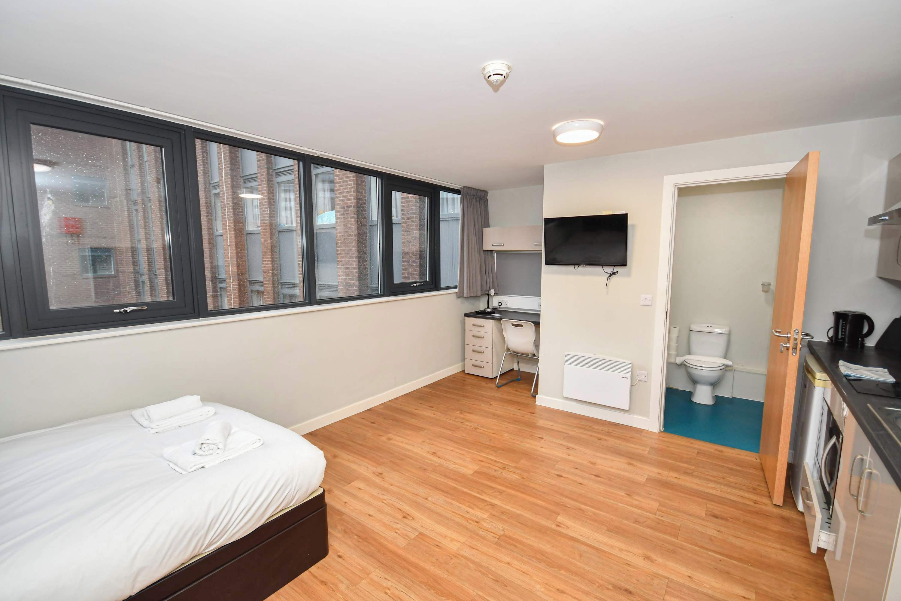 Een slaapkamer met een groot raam, een bed, een bureau, een televisie en een badkamer.