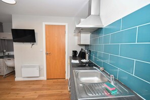 A kitchen with a sink, a stove, a microwave, and a television mounted on the wall. - Convenient Budget Studio in Central Sheffield (Sheffield)