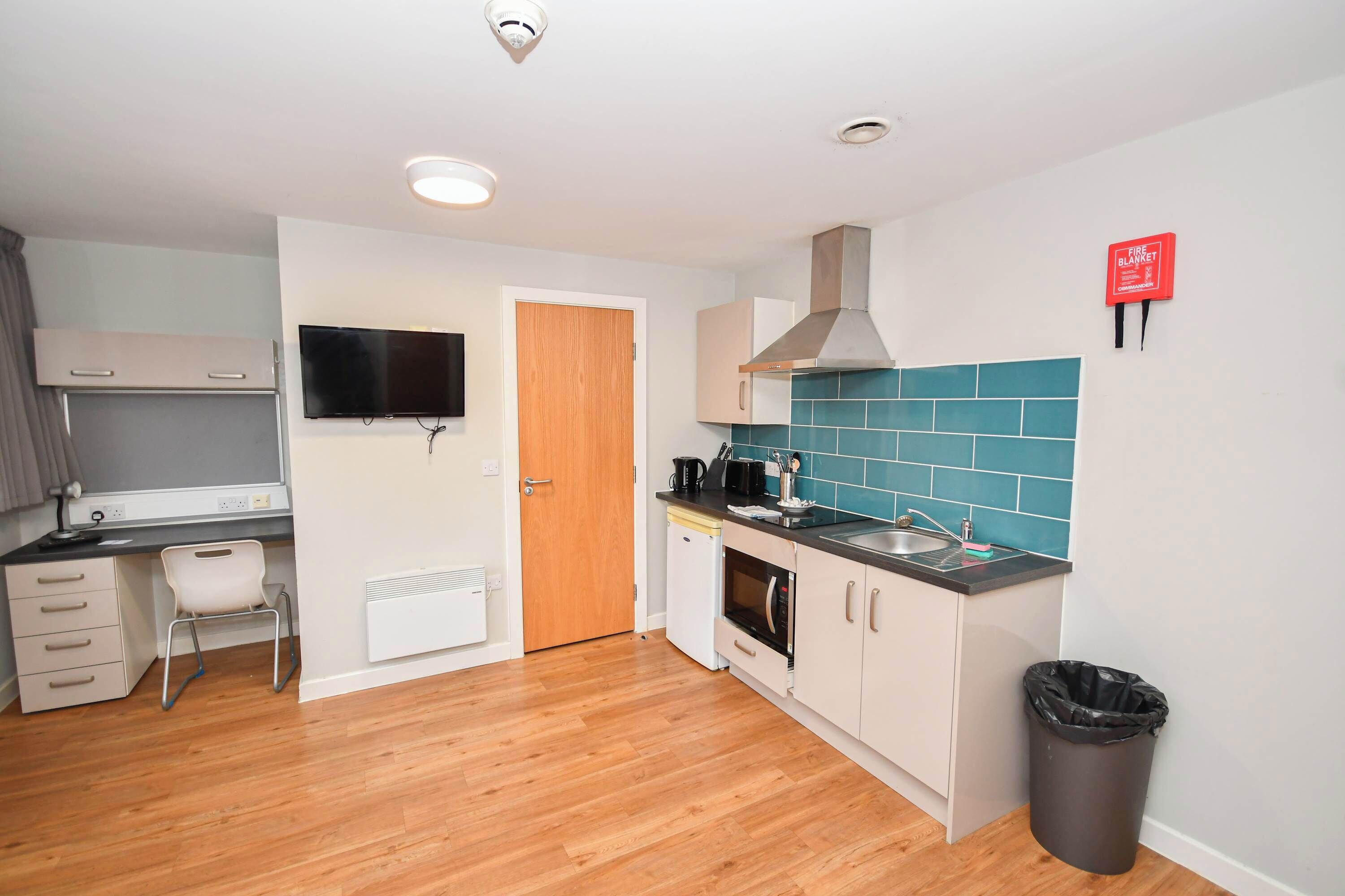 A compact kitchen with a microwave, stove, sink, and a fire blanket sign.