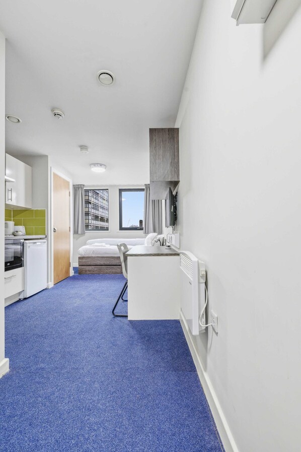 A compact hotel room with a kitchenette, a bed, a small desk, and a window with a view of buildings. - Modern Budget Single Studio in Central Nottingham (Nottingham)