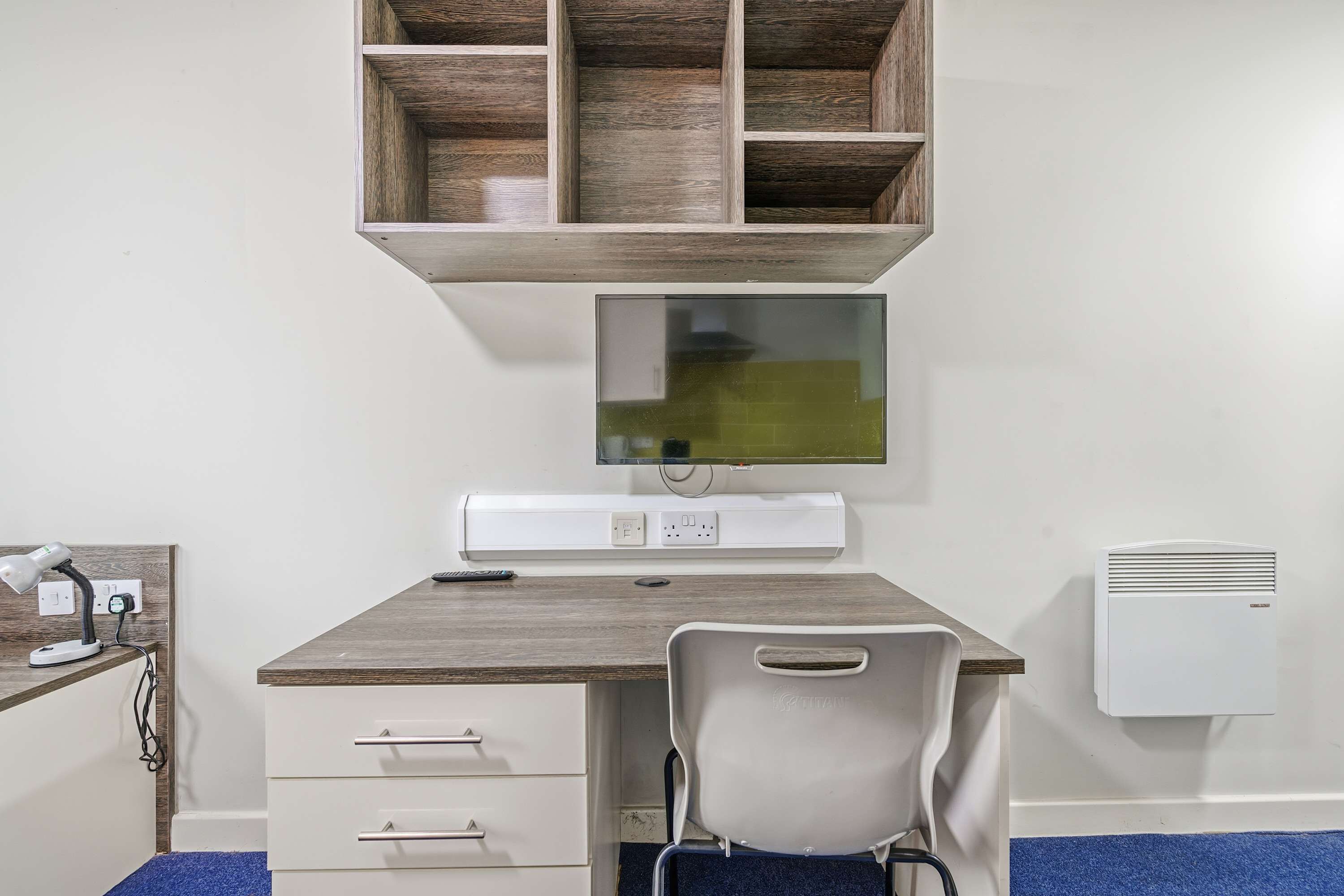 A room with a desk, chair, shelf, and wall-mounted air conditioner.