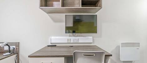 A room with a desk, chair, shelf, and wall-mounted air conditioner.