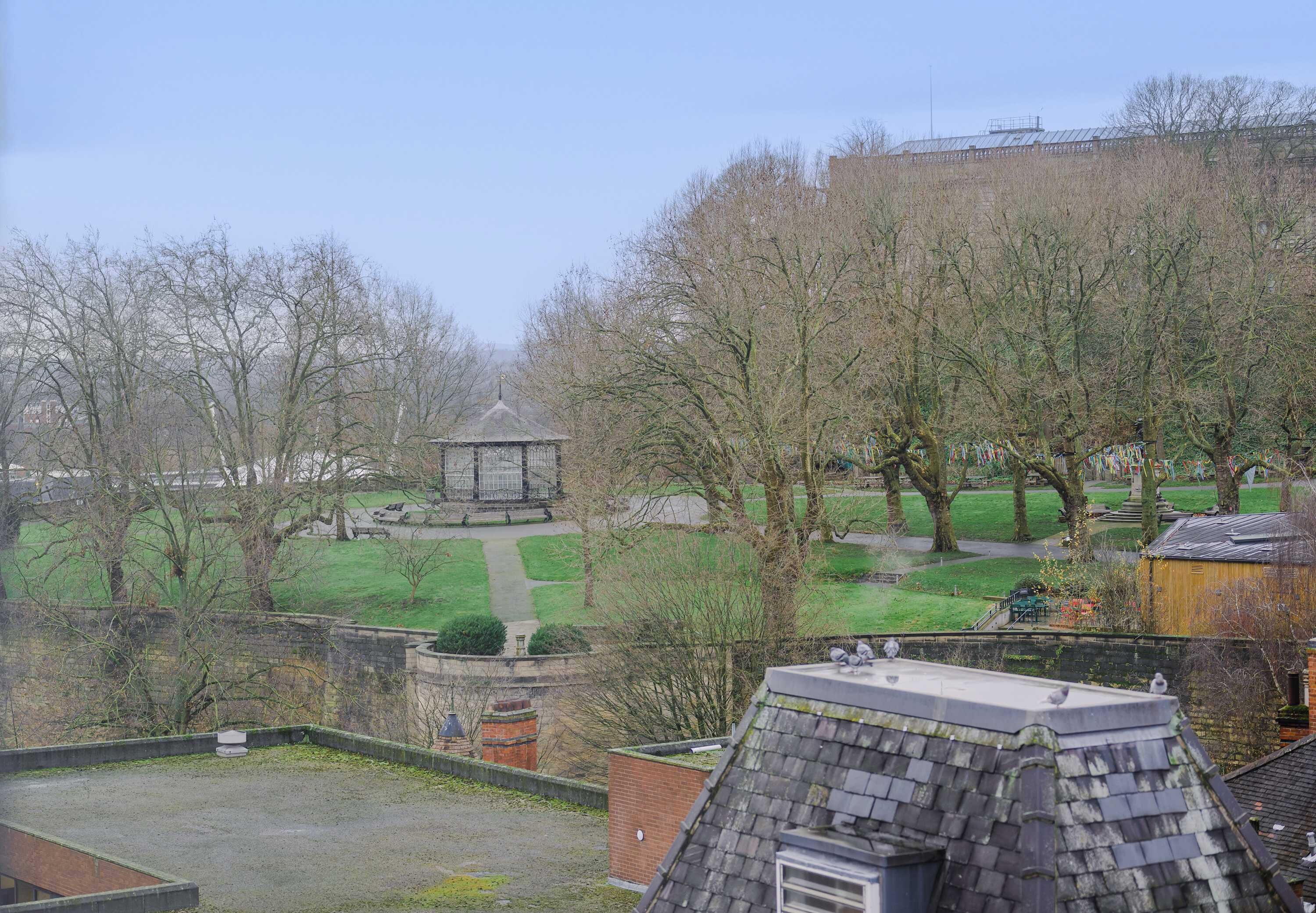 A view of a park with a gazebo, trees, and a building in the background.