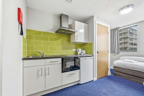 A compact kitchen with white cabinets, a microwave, and a built-in oven. - Modern Budget Single Studio in Central Nottingham (Nottingham)