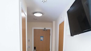 A hallway with wooden flooring, white walls, a door with a sign, and a mounted television. - Cosy Budget Single Studio in Central Nottingham (Nottingham)