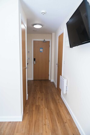 Ein Flur mit Holzboden, weißen Wänden, einer Tür mit einem Schild und einem an der Wand befestigten Fernseher.