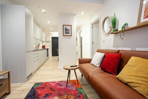 A modern living room with a brown leather sofa, colorful rug, and a small round table. - Contemporary 2 Bed Apartment in Central Manchester (Manchester)