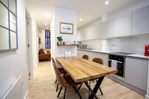 A modern kitchen with white cabinets, a wooden dining table, and a red kettle. - Contemporary 2 Bed Apartment in Central Manchester (Manchester)