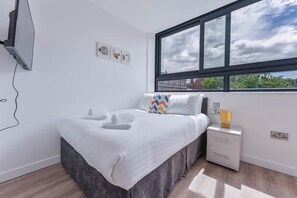 A bedroom with a bed, a window, a bedside table, and a wall-mounted TV. - Modern and Bright Studio in Central Sheffield (Sheffield)