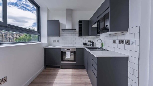 Eine moderne Küche mit dunklen Schränken, einem Edelstahlbackofen, einer Mikrowelle und einem Fenster mit Blick auf Gebäude.