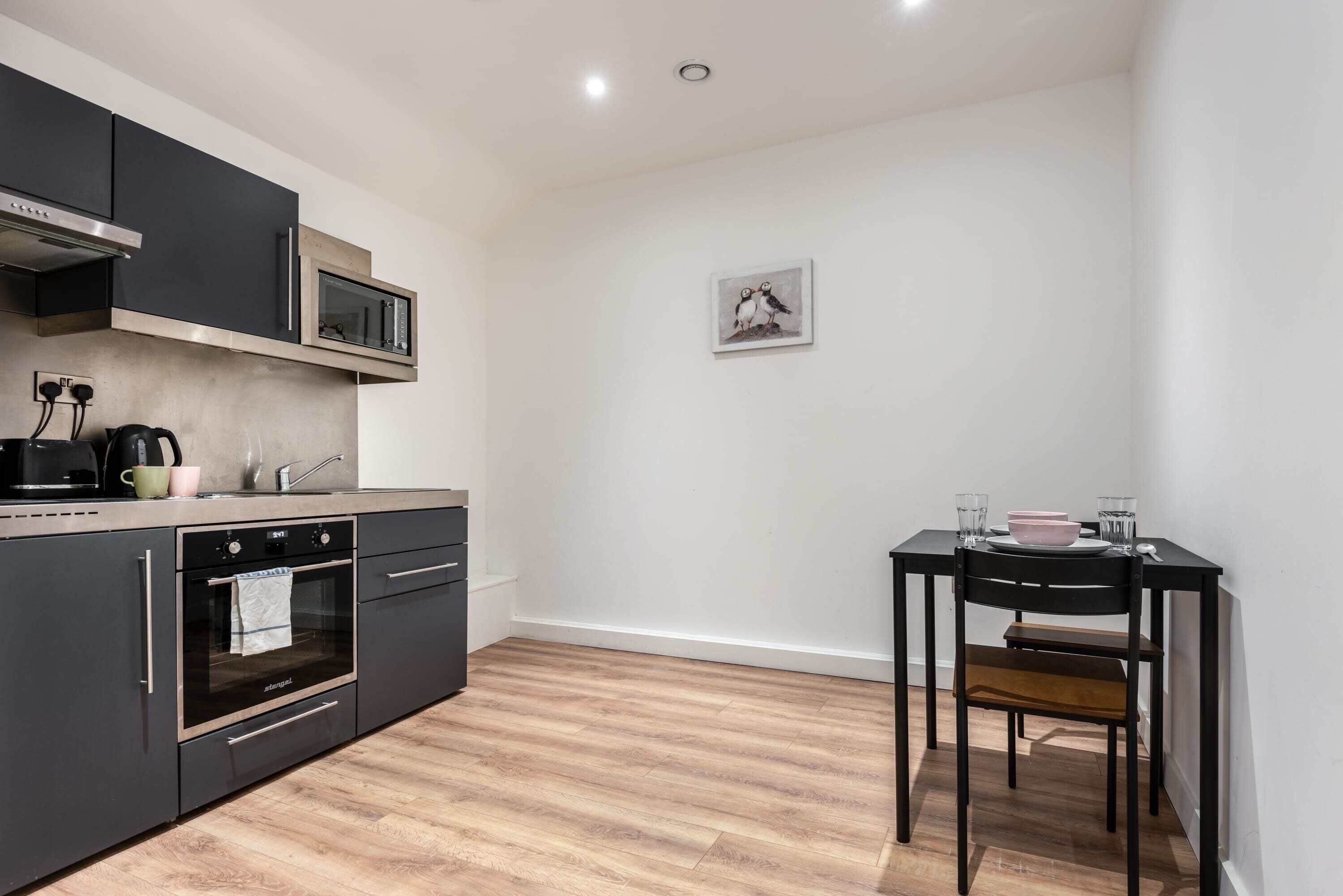 A modern kitchen with built-in appliances, a dining table with chairs, and a picture on the wall.