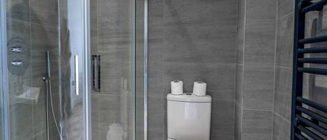 Un baño moderno con cabina de ducha de vidrio, inodoro y toallero.